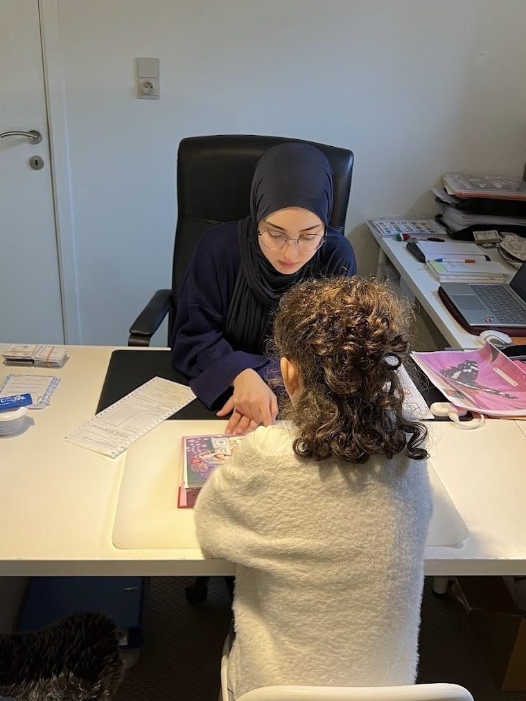 Fatma Ciçek werkt aan de werktafel samen met een kind aan een taaloefening.