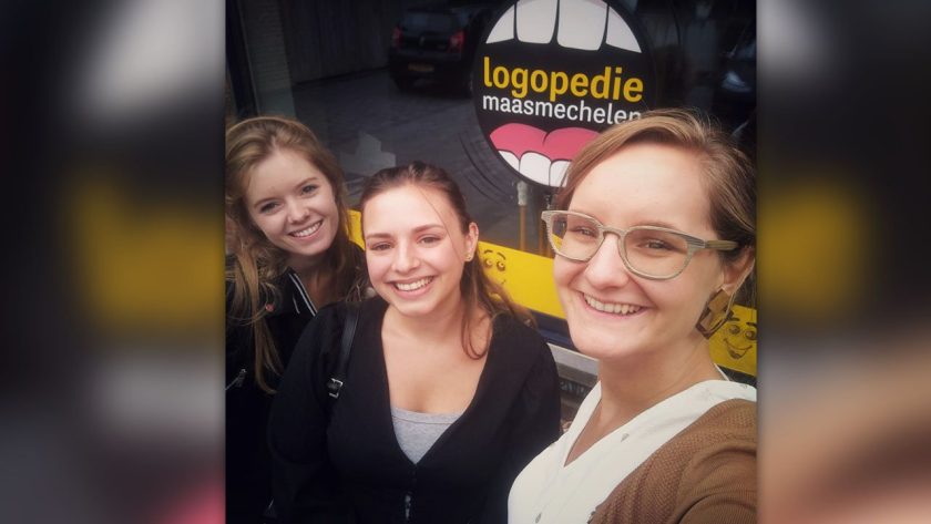 Drie logopedisten van de praktijk voor het raam met de raamsticker.
